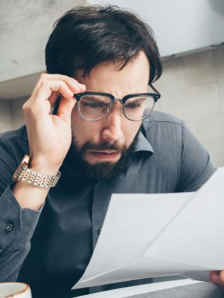 Man with glasses scrutinizing financial papers, showing concern.